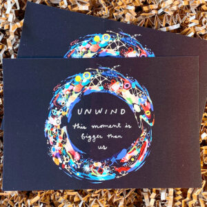 two postcards on brown crinkle paper that say "unwind this moment is bigger than us" with an illustrated ouroboros