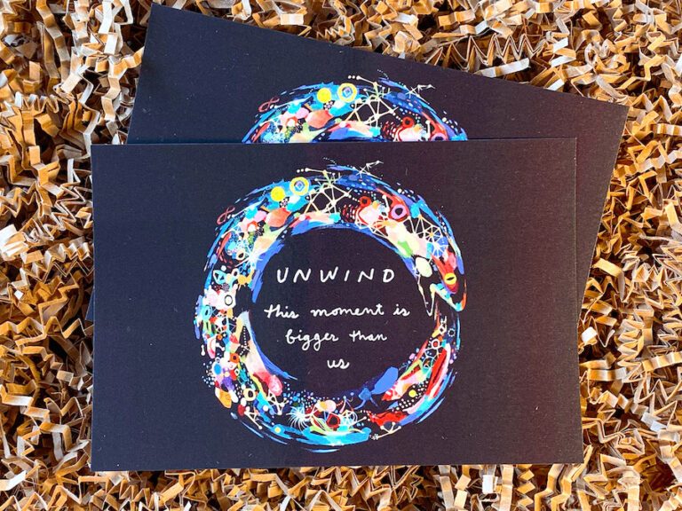 two postcards on brown crinkle paper that say "unwind this moment is bigger than us" with an illustrated ouroboros